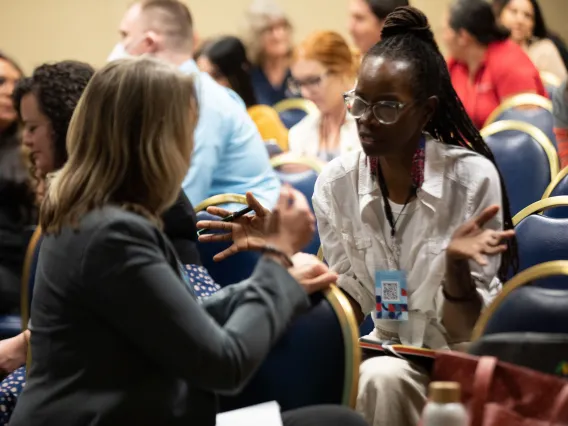 Two women in a discussion, seated in a conference audience.